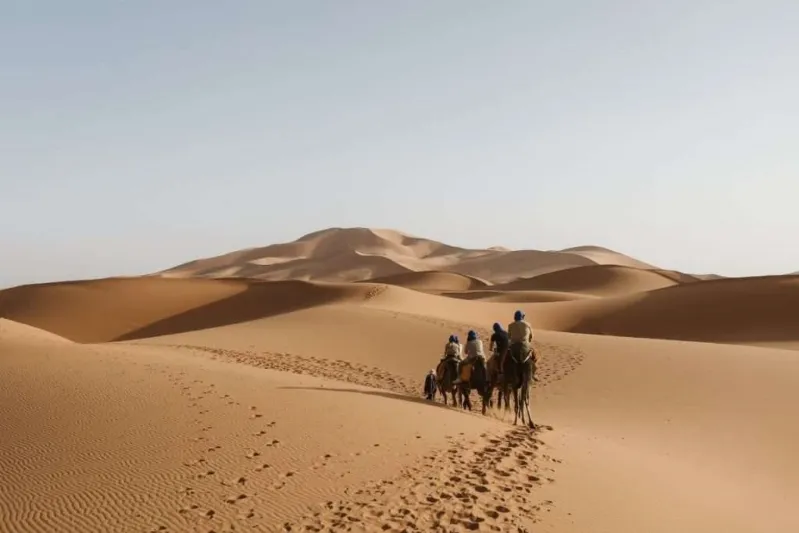 A group of riders on camels traversing sandy desert dunes.
